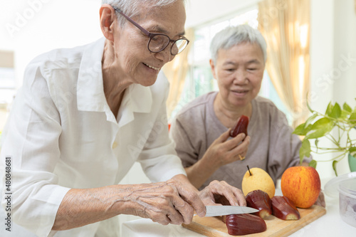 Happy asian senior grandmother cutting the fresh fruit into slices with a knife,healthy elderly people enjoy tasting delicious fruits,preparing healthy meal,cooking,healthy  food,health care concept
