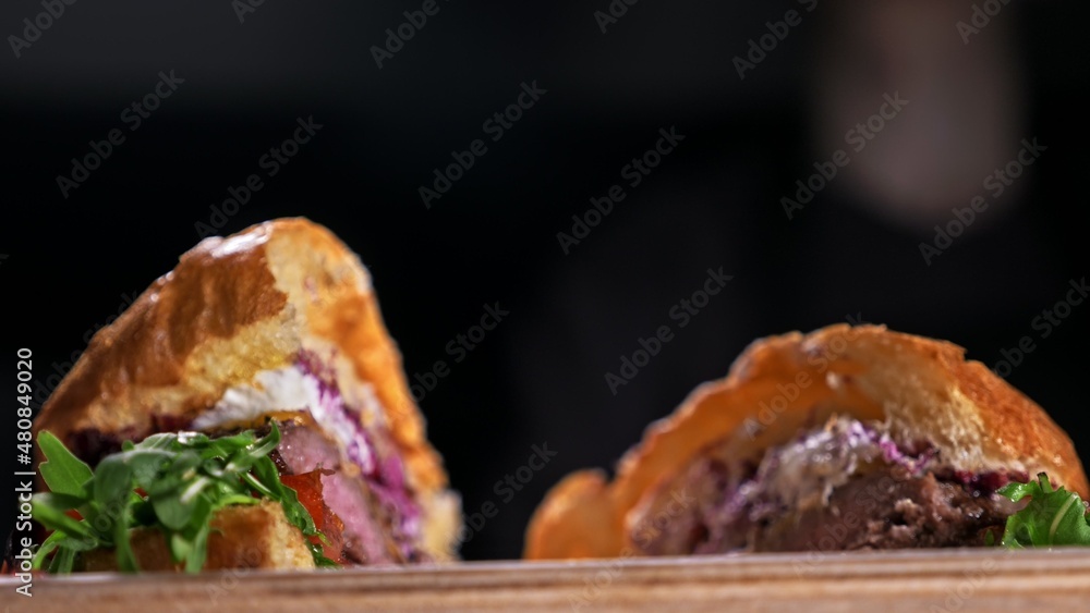 Cut craft burger is cooking on black background. Consist: sauce, lettuce, tomato, red onion, pickle, cheese, bacon, air bun and marbled meat beef. Cut craft burger is cooking on black background. Consist: sauce, lettuce, tomato, red onion, pickle, cheese, bacon, air bun and marbled meat beef.