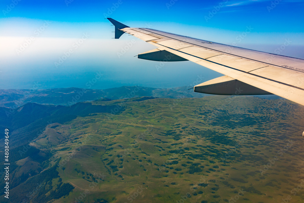 View of airplane wing, blue skies and green land during landing. Airplane window view. View of airplane wing, blue skies and green land during landing. Airplane window view.