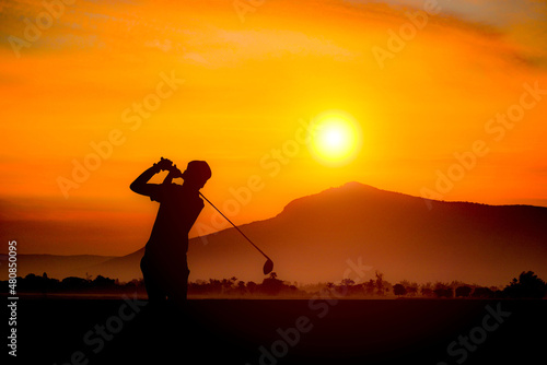 Golfers' hit golf ball toward the hole at sunset silhouetted