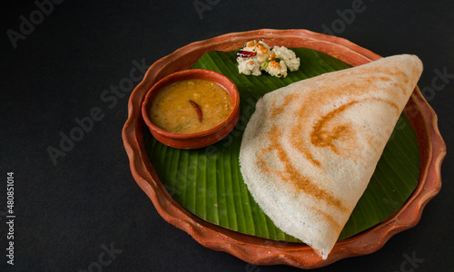 traditional south indian food masala dosa, sambar and coconut chutney served on clay plate and banana leaf. studio shot. photo