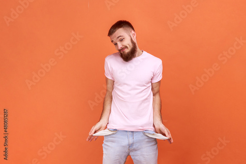 Foto Portrait of bearded man showing empty pockets and looking frustrated about loans and debts, has no money, jobless, wearing pink T-shirt