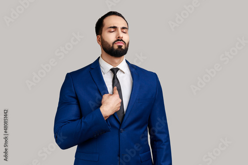 Portrait of bearded man pointing himself and looking selfish egoistic haughty, feeling proud of own achievement, wearing official style suit. Indoor studio shot isolated on gray background. photo