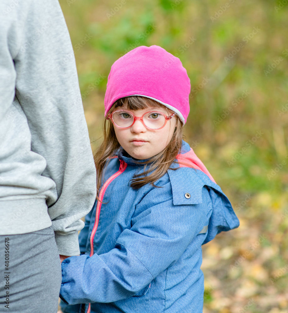 Mother and little girl with Downs syndrom walk in autumn park