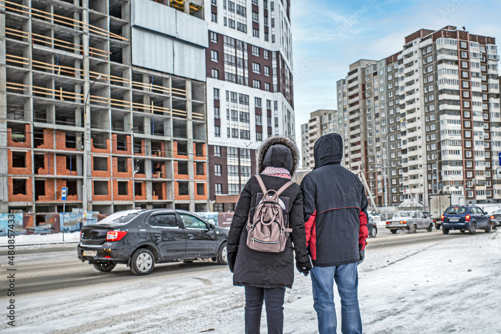 A man and a woman look at a residential building under construction on a winter day