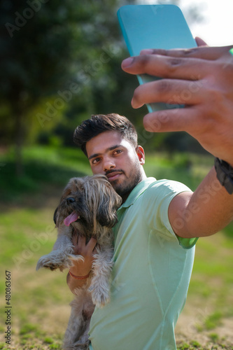 Portrait of young man with dog on the park, taking selfie © paltu