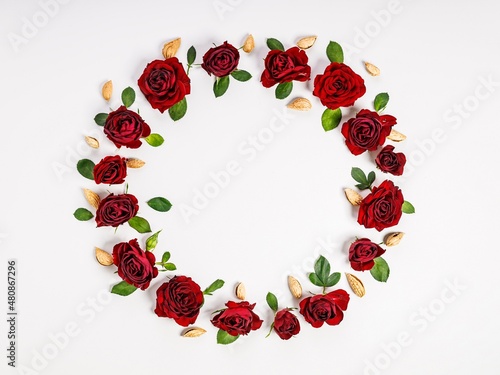Wreath in the form of a ring of red roses, green leaves and almonds. Composition on a light background. Top view