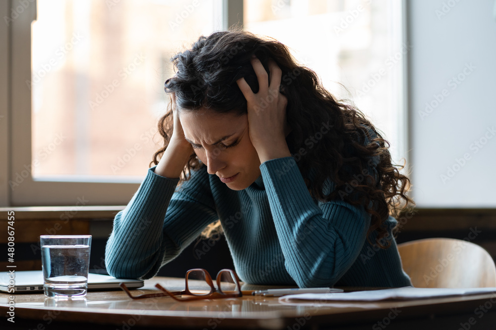 © DimaBerlin - Unhappy female overworked and stressed sit at desk with closed laptop suffer from headache, depression feeling exhausted frustrated with bad news, failure at work. Tired sick woman worker in office