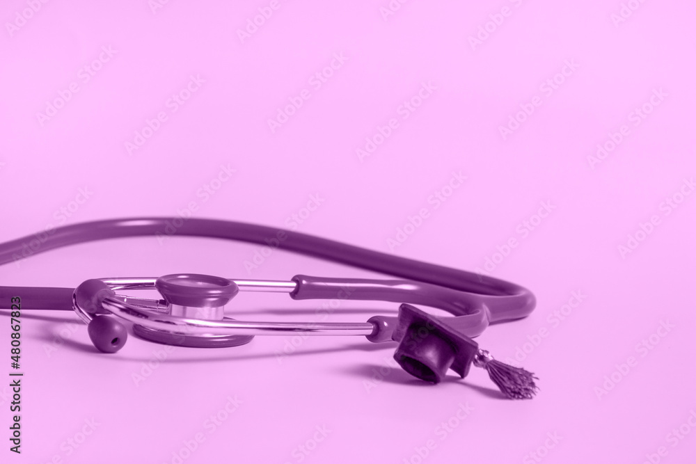 Fototapeta premium Graduation cap with stethoscope and numbers 2022 on violet background, closeup with copy space. Medical education concept.