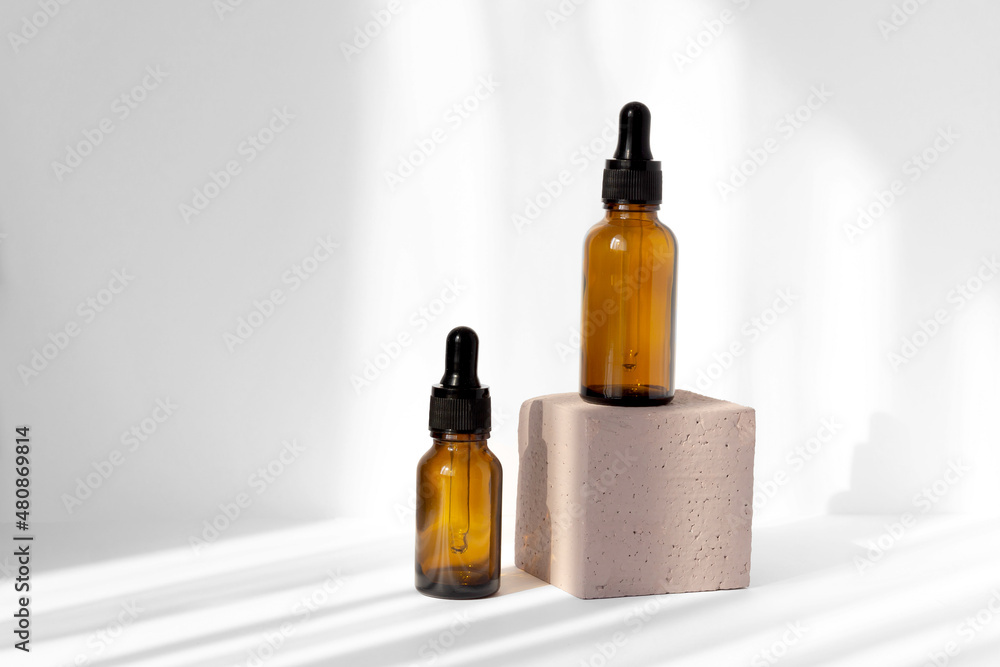 Mock-up of two bottles with dropper lids on white background in rays of sunlight, located on square stand. Concept of 3d podium for demonstration of beauty products