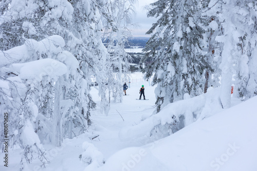 Snowboarders behind snowy trees in a skiing resort in Finland