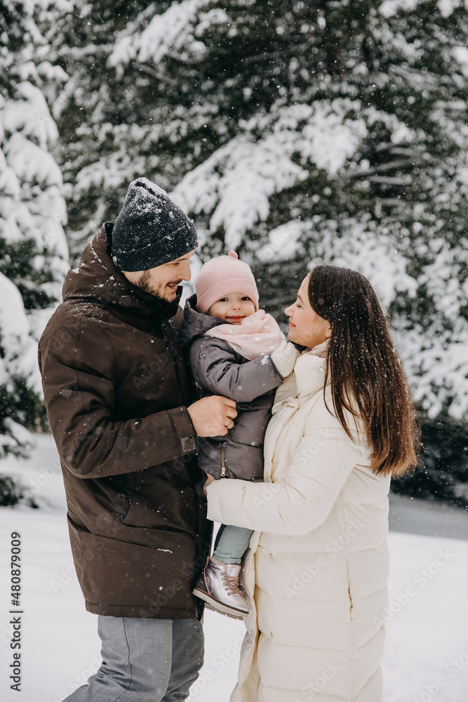 Mother and father holding little girl in arms outdoors on a snowy winter day in mountains. Mother and father holding little girl in arms outdoors on a snowy winter day in mountains.