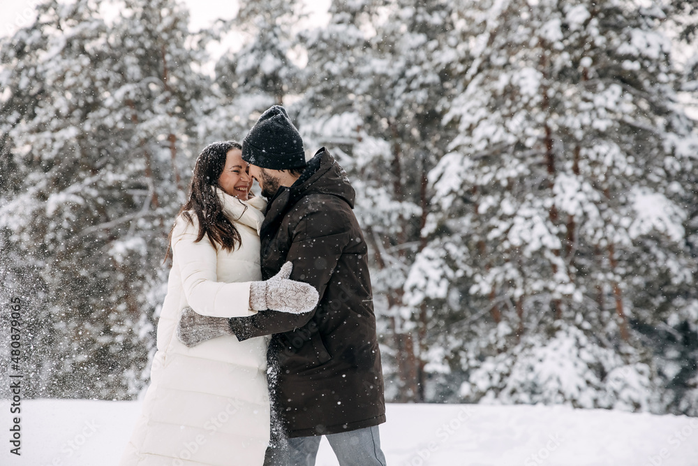 Happy couple spending time outdoors, hugging and smiling on a cold snowy winter day.