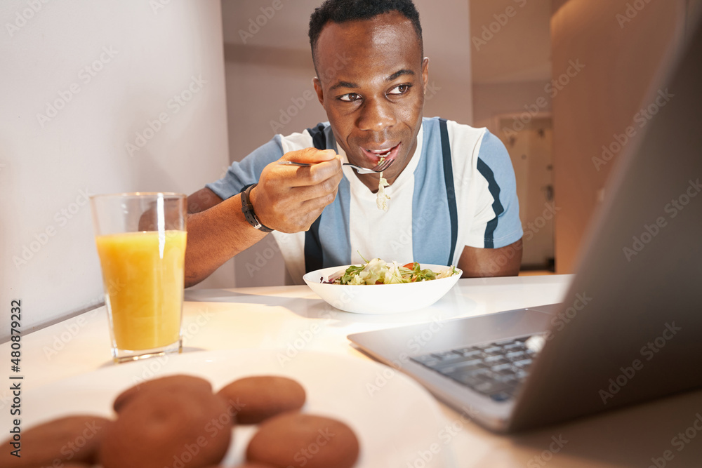 Multiracial man is eating meal before laptop Multiracial man is eating meal before laptop