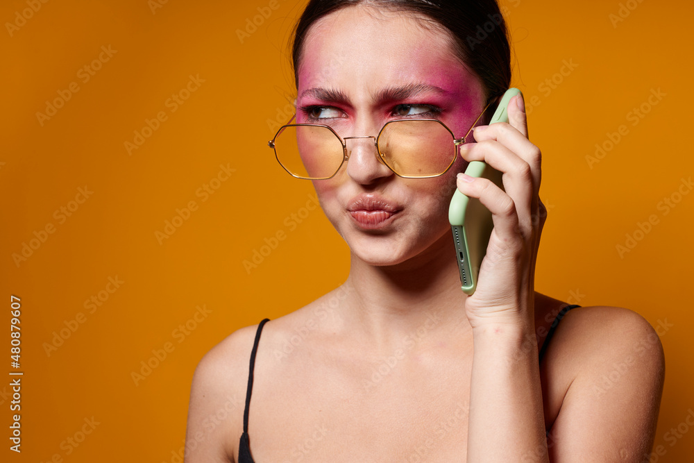 fashionable woman with phone pink face makeup posing attractive look glasses yellow background unaltered fashionable woman with phone pink face makeup posing attractive look glasses yellow background unaltered
