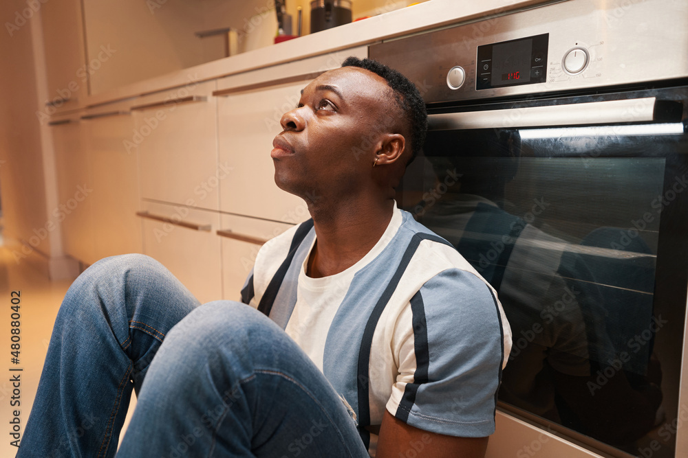 Upset man looking up while sitting near stove Upset man looking up while sitting near stove