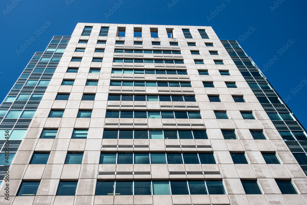 Angled view of a large, window covered apartment building corner against a blue, cloud filled sky Angled view of a large, window covered apartment building corner against a blue, cloud filled sky