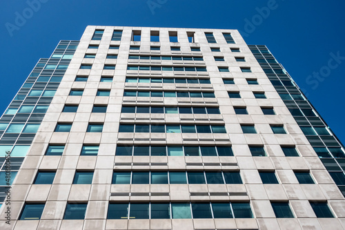 Angled view of a large, window covered apartment building corner against a blue, cloud filled sky