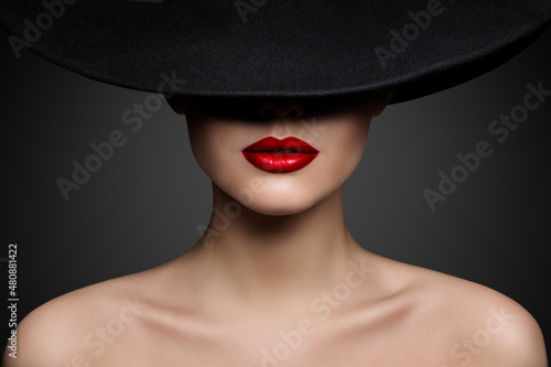 Red Lips Make up Closeup. Mysterious Fashion Woman Face Hidden by Black brimmed Hat. Elegant Retro Lady Fine Art Portrait over Gray Background © inarik