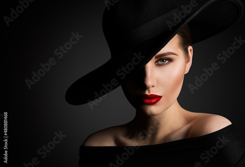 Elegant Woman Face Portrait hidden by Black Hat. Beauty Fashion Model with Red Lips and Eye Make up over dark Gray Background photo