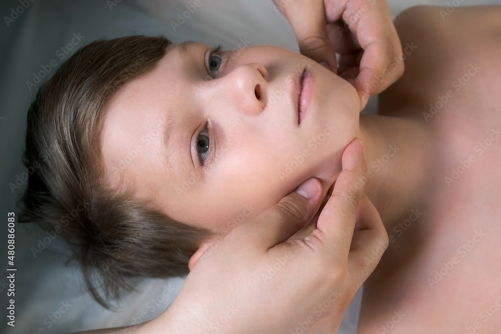 Session of craniosacral therapy, cure of teen boy's jaw and neck by a doctor therapist. Craniosacral therapist touches the boy's cheeks and checks the correctness of the jaws at the hospital.