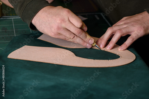 Obraz na płótnie Shoemaker hands holding craft knife cutting green suede leather for handmade shoes on his workplace in workshop. Closeup. Copy space. w salonie