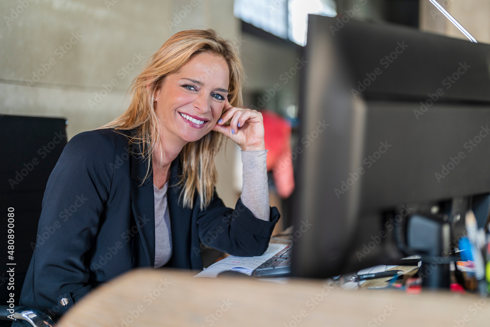 Smiling businesswoman leaning on hand at desk in office Smiling businesswoman leaning on hand at desk in office
