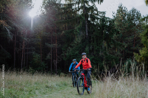 Active senior couple riding bikes outdoors in forest in autumn day.