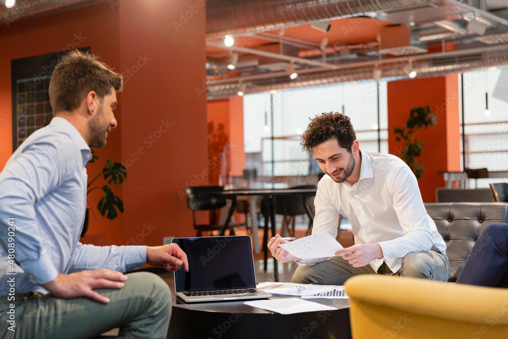 Businessman reading document sitting with colleague in office Businessman reading document sitting with colleague in office