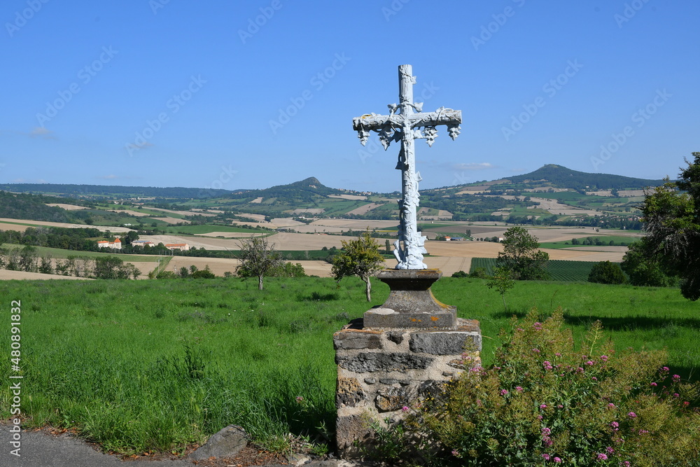 Croix de pierre avec des sculptures de raisins surplombant une vallée verdoyante dans le puy de dôme