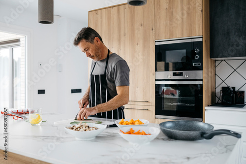 Man wearing apron cutting vegetables in kitchen at home photo