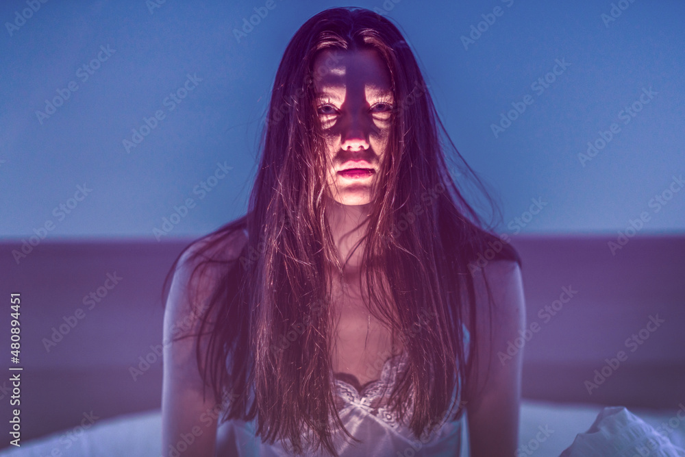 Scare. Horror. Scary girl with dark hair. The woman shines a flashlight at herself from below and creates a scary face - obrazy, fototapety, plakaty 