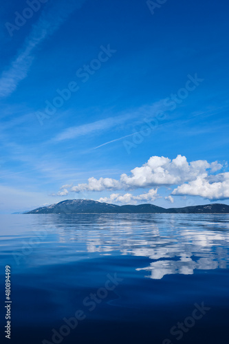 blue sky with clouds and island with water reflection