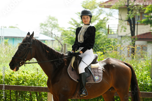 Young 20s Asian woman in horse riding suit with beautiful animal outdoors. Female ride tall smart © Jade