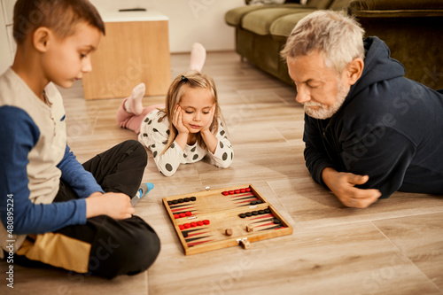 Boy and girl playing backgammon with grandfather at home photo