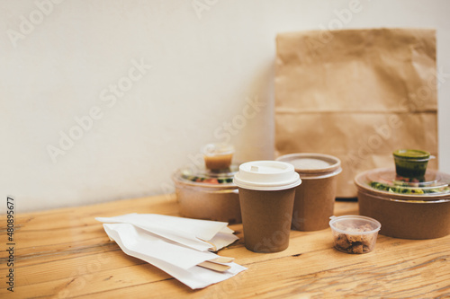 Takeaway food in containers and disposable bowls on wooden table on white background. Food delivery and takeout. Place for text.