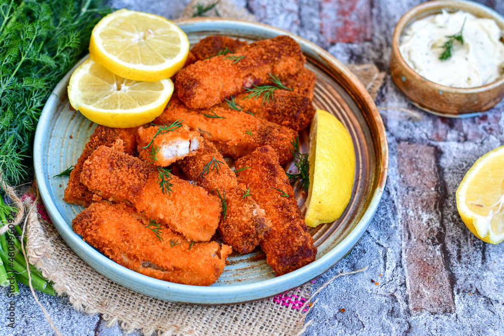 Close up of Crispy breaded deep fried fish fingers with breadcrumbs served with remoulade sauce and lemon Cod Fish Nuggets on rustic wood table background Close up of Crispy breaded deep fried fish fingers with breadcrumbs served with remoulade sauce and lemon Cod Fish Nuggets on rustic wood table background