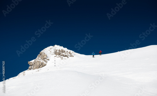 Two mountaineers are hiking on top of the mountains during a winter sunny day with blue sky. Trekking sport in nature.