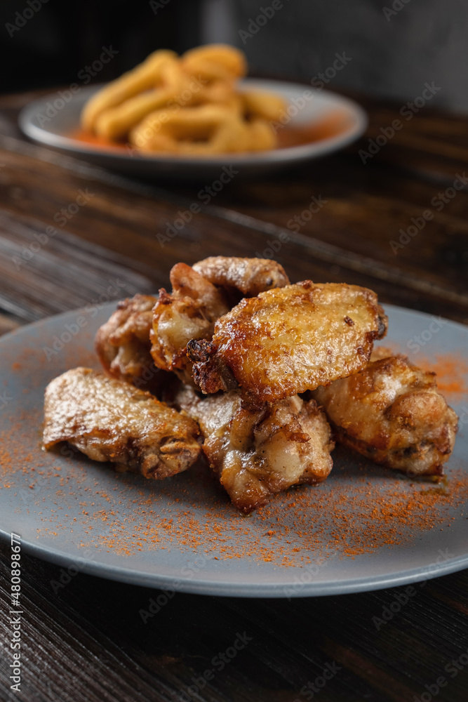 Spicy fried chicken wings in a plate on a wooden table sprinkled with spices. Vertical orientation, copy space, no people, close-up, dark moody Spicy fried chicken wings in a plate on a wooden table sprinkled with spices. Vertical orientation, copy space, no people, close-up, dark moody