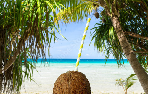 summer holidays, travel and tourism concept - close up of coconut drink with paper straw over tropical beach background in french polynesia