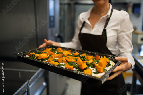 Cut out of unrecognizable female cook holding tray with baked pumpkin pieces in commercial kitchen.