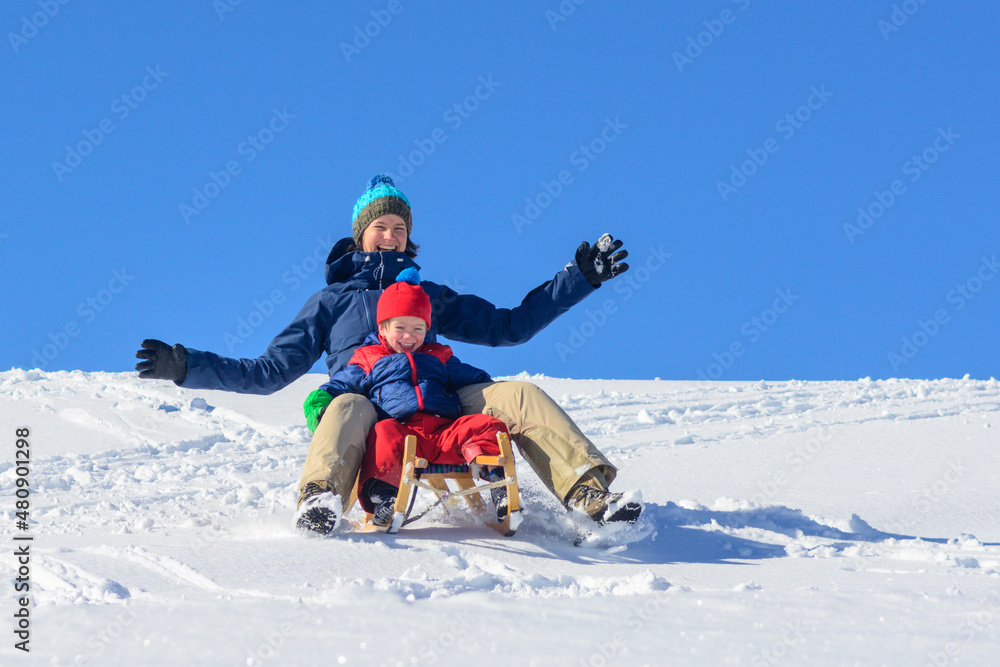 Mutter und Kind haben Spass beim Rodeln an einem sonnigen Wintertag Mutter und Kind haben Spass beim Rodeln an einem sonnigen Wintertag