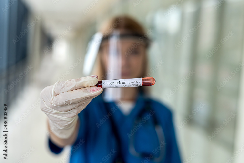 a young nurse in a uniform with a protective cap holds a blood sample on a covid a young nurse in a uniform with a protective cap holds a blood sample on a covid