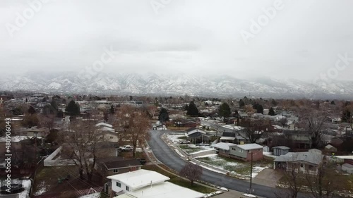 An aerial drone shot tracking backwards over a residential area, in the distance a spectacular view of the Wasatch Mountains covered in snow on a cold gloomy winter’s day, Layton, Utah photo