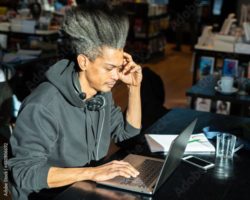 young afro american man studying new content for his personal blog, young latin american working on project connected with modern tecnologies, lifestyle concept of connected working people © MandriaPix