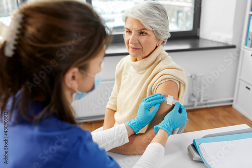 medicine  health and vaccination concept - doctor or nurse applying medical patch to vaccinated senior woman at hospital