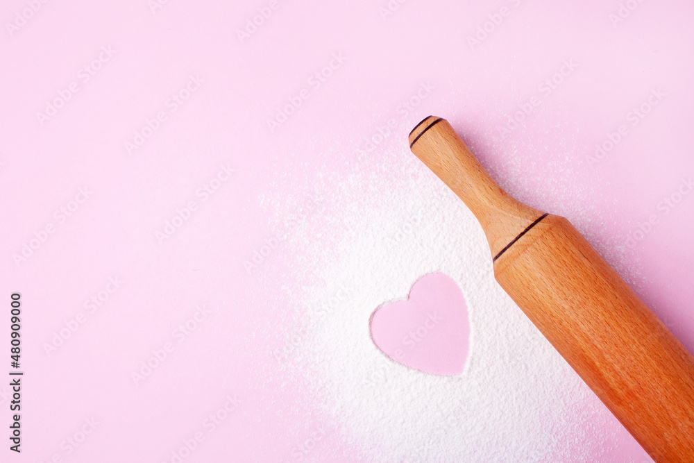 Rolling pin, flour and heart on a pink background. Cooking cookies for valentine's day. Top view