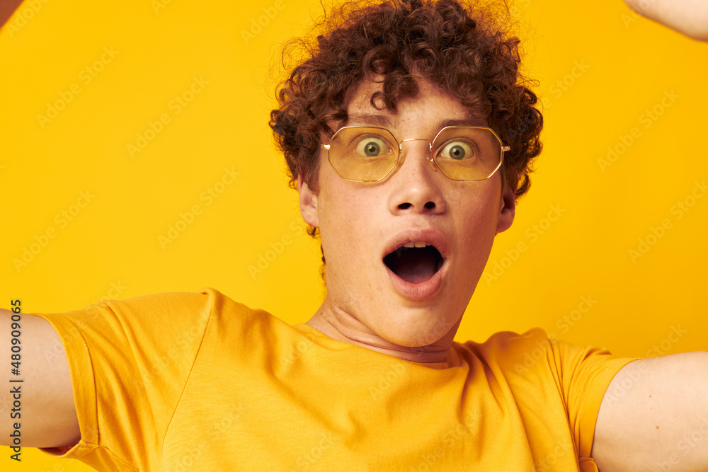 Young curly-haired man yellow t-shirt glasses fashion hand gestures isolated background unaltered Young curly-haired man yellow t-shirt glasses fashion hand gestures isolated background unaltered