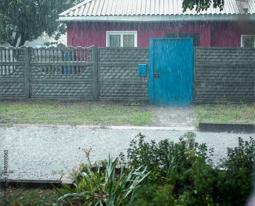 Heavy rain with puddles and old village house with concrete fenc photo