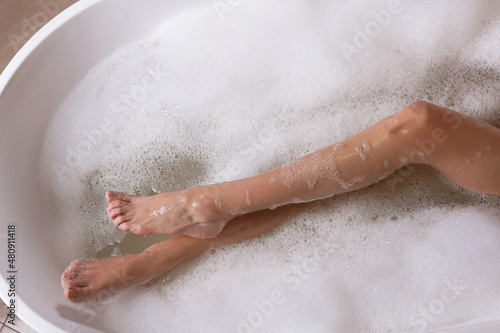 Woman taking bath with shower gel in tub, top view